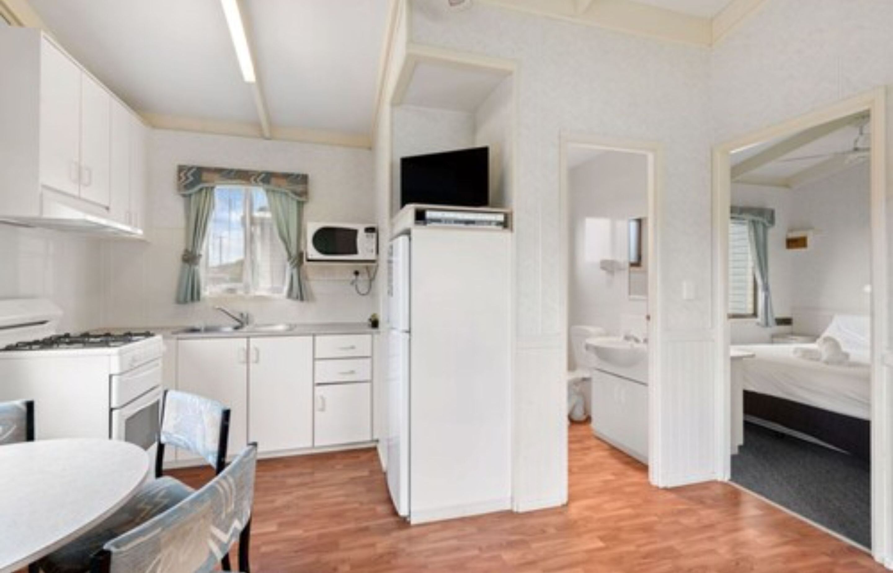 Una cocina funcional con armarios blancos, microondas, refrigerador y un comedor con mesa y sillas.