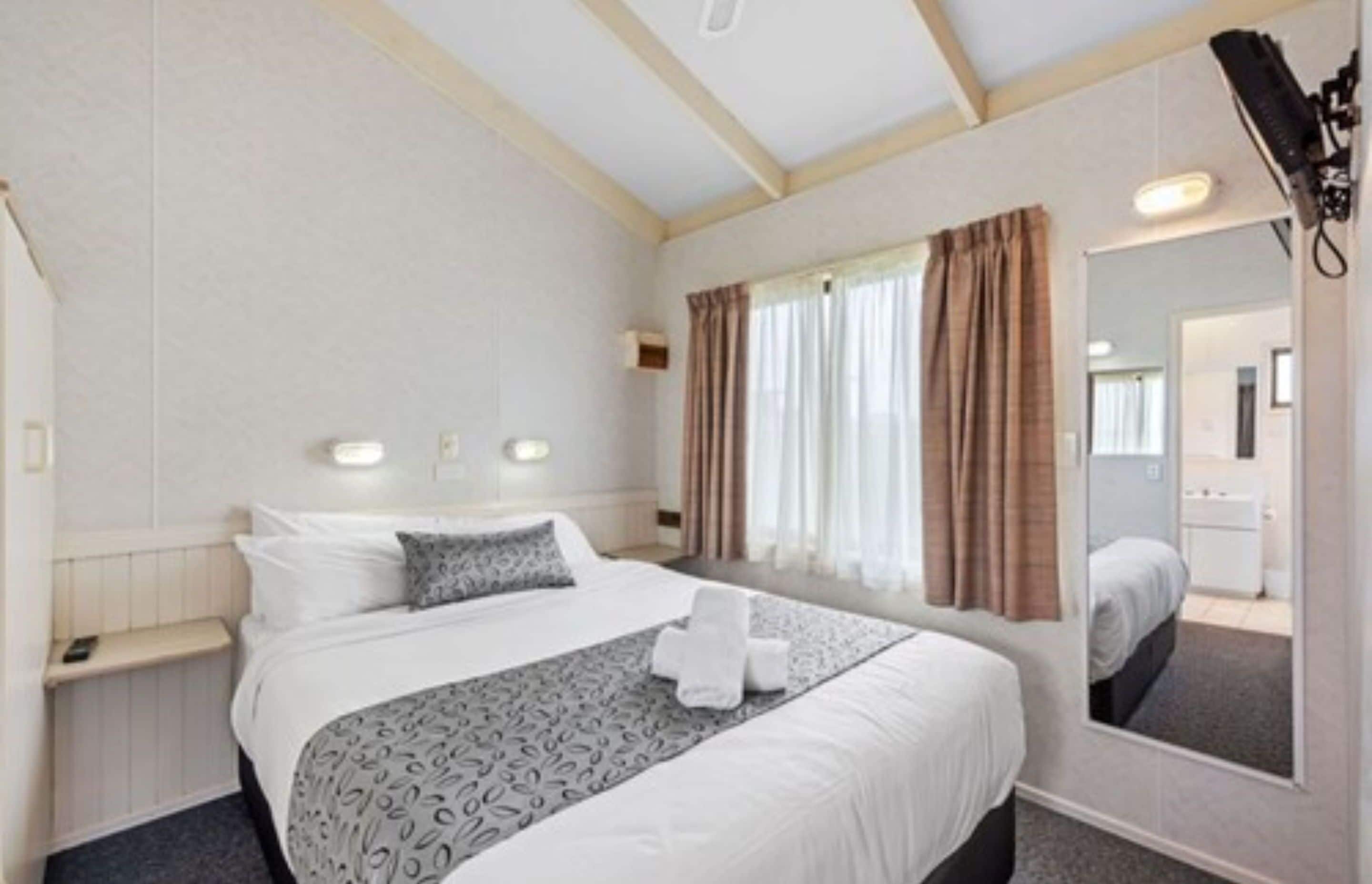 A hotel room with a large bed, bedside tables, a mirror, and a window with curtains.