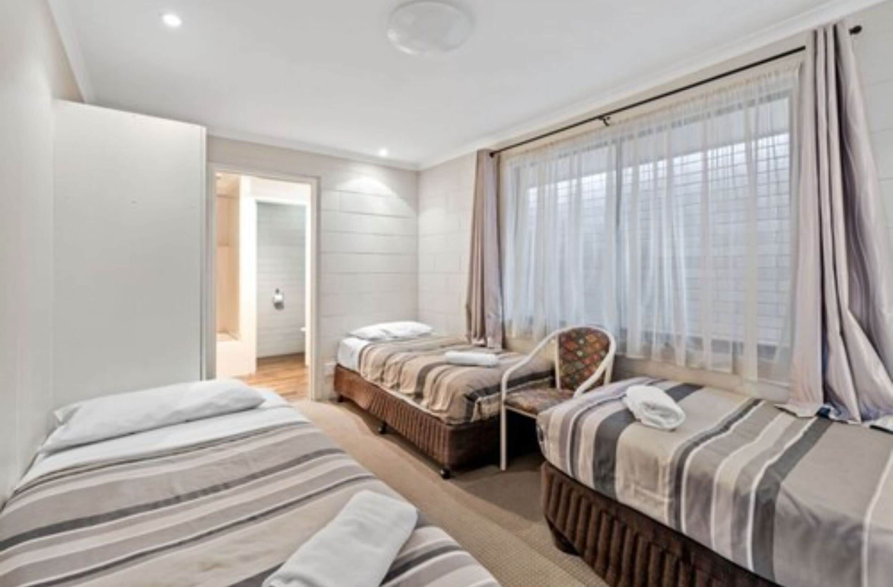 A bedroom with two beds, a chair, and a window with curtains.