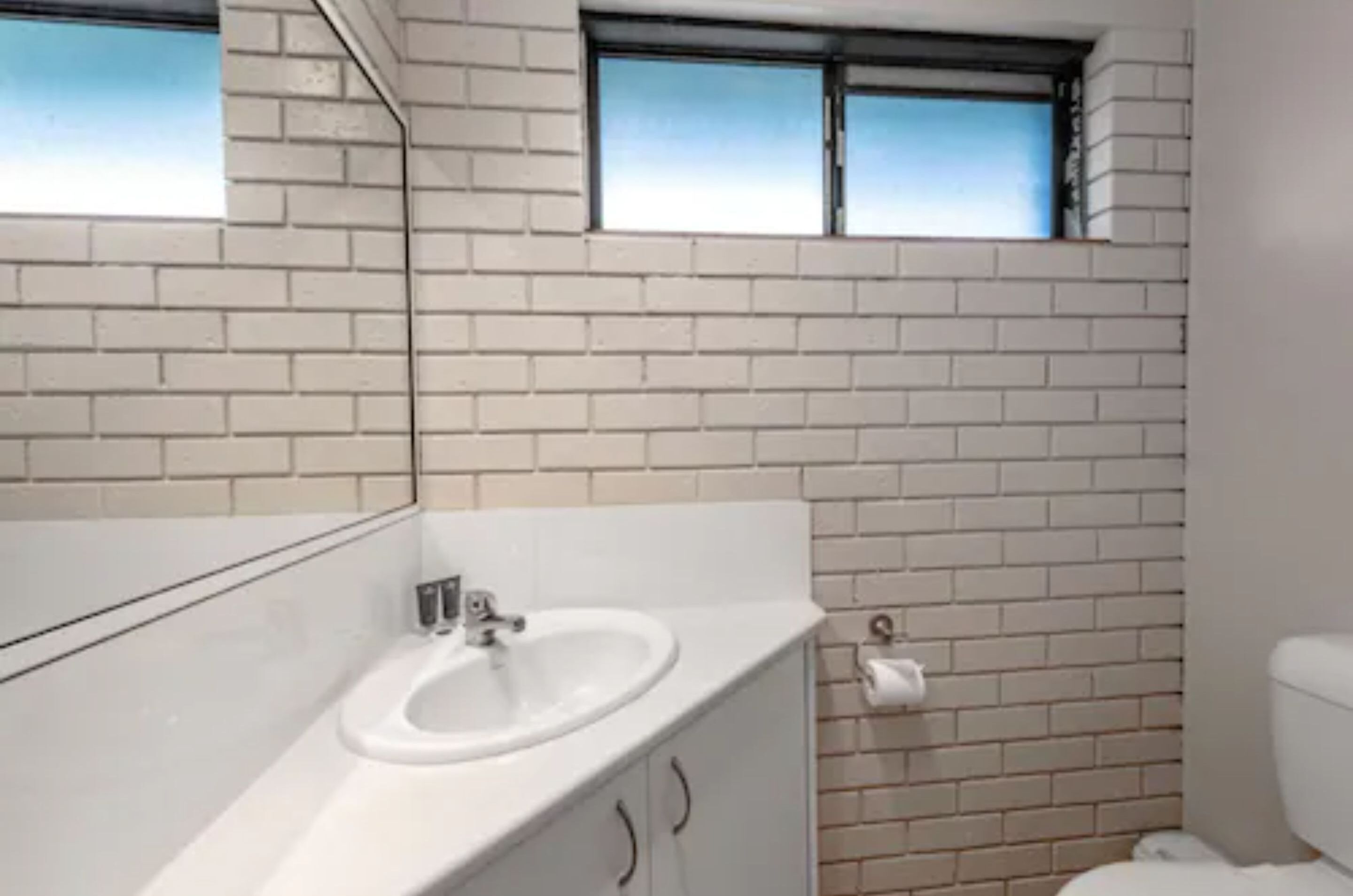 A bathroom with a white sink, a mirror, and a window above the sink.