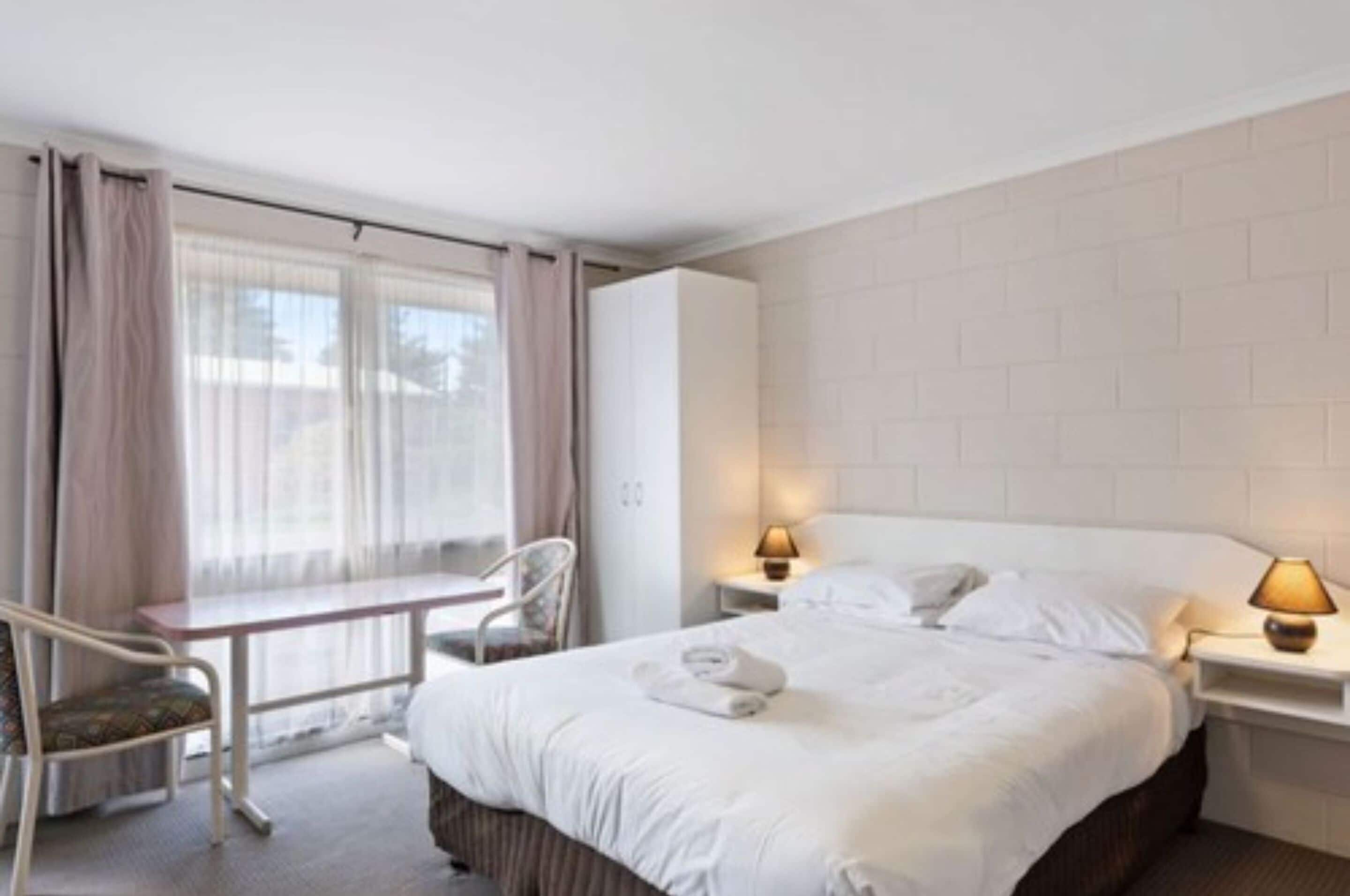Una habitación de hotel con cama, lámparas de noche, escritorio y silla.