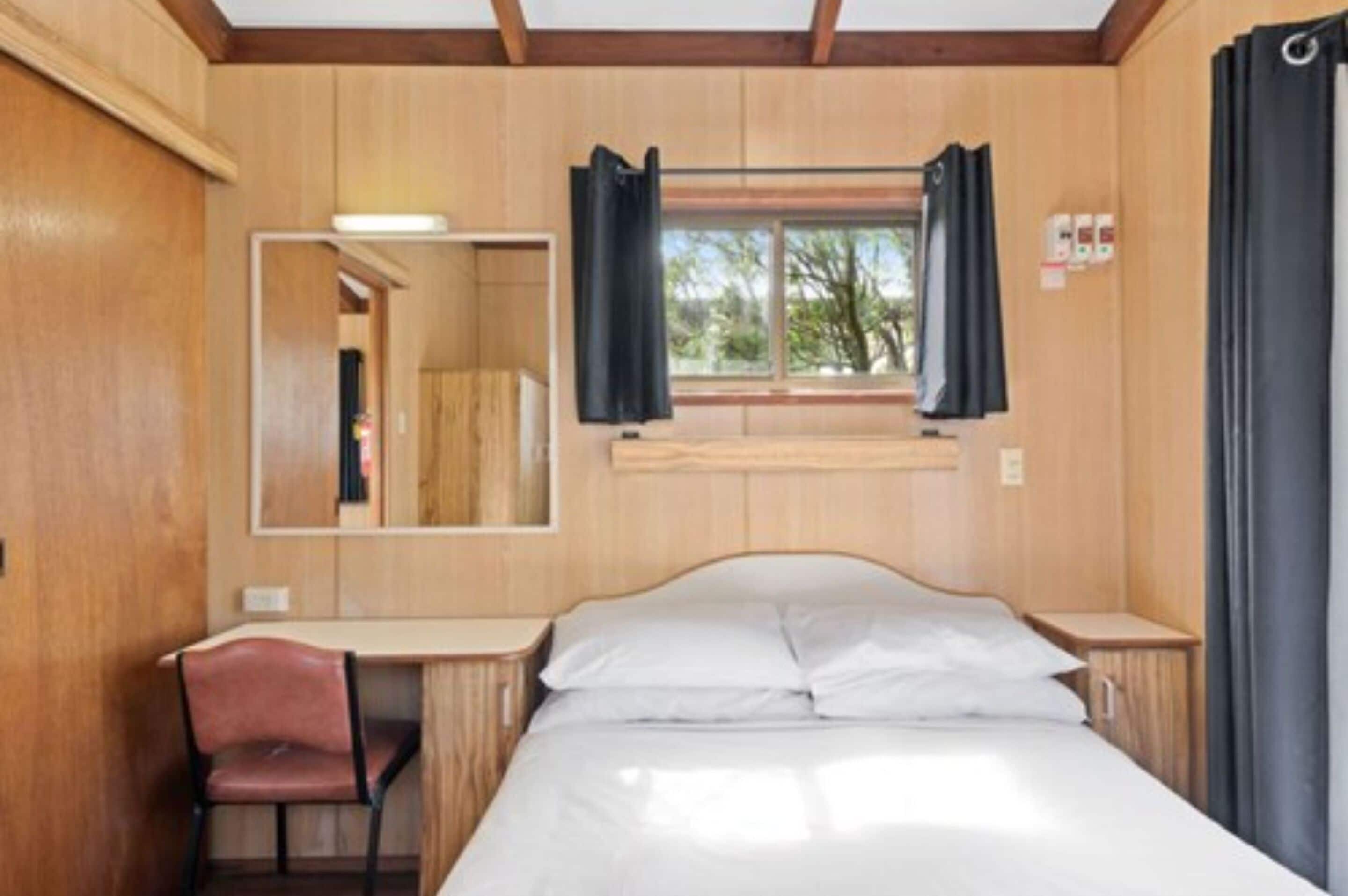A room with a bed, a desk, and a chair. There is a window with curtains.