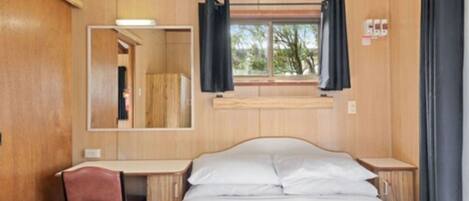 A room with a bed, a desk, and a chair. There is a window with curtains.