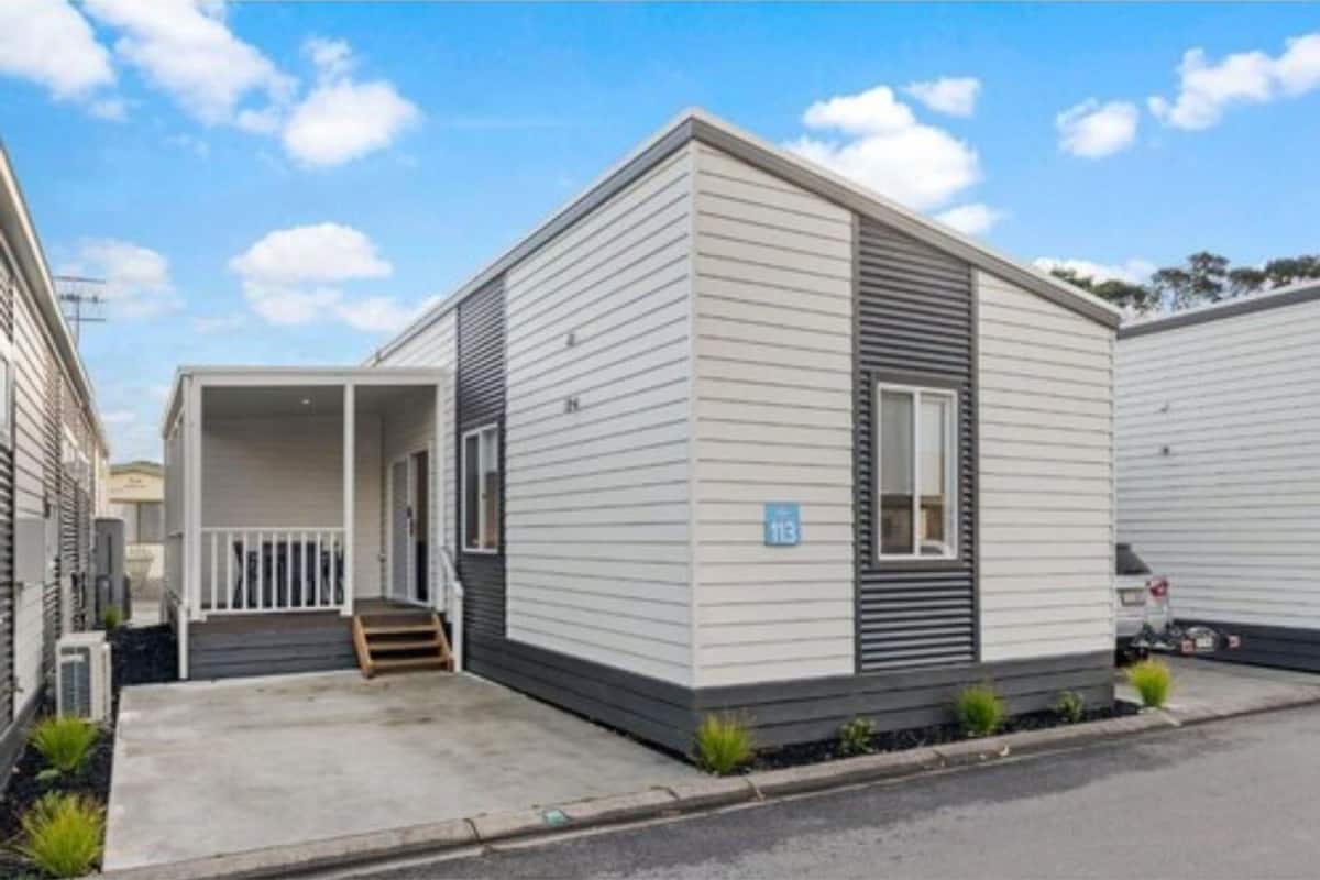 A single-story mobile home with a front porch, a small front yard, and a visible address number.