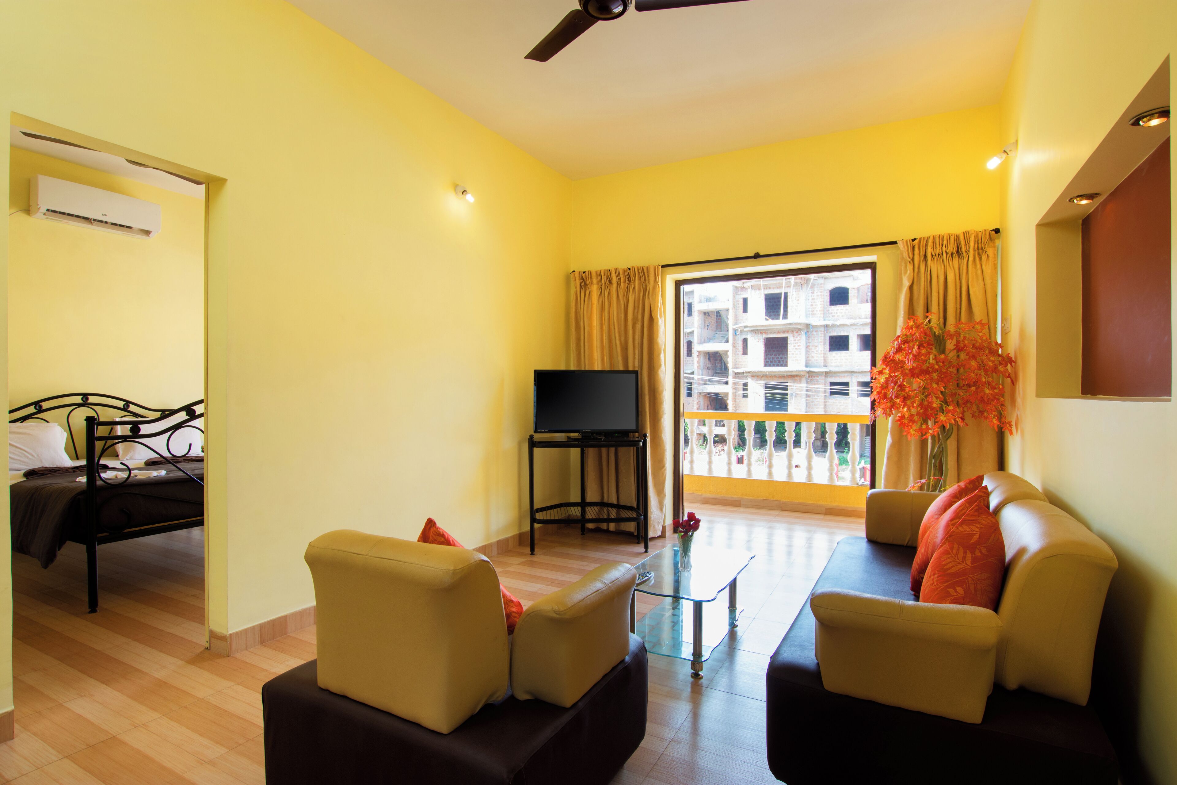 A living room with a sofa, a television, and a balcony with a view of buildings.