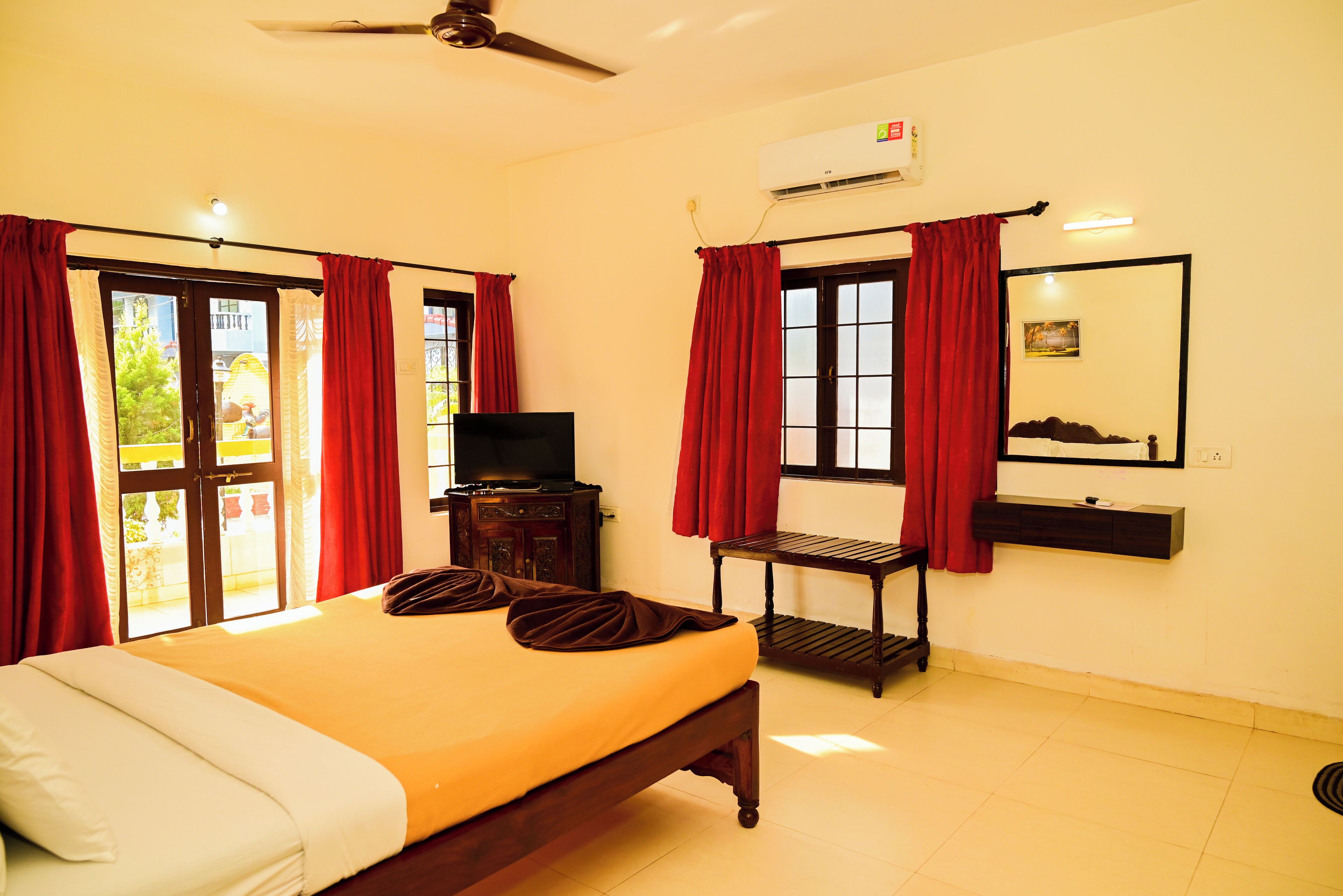 A hotel room with a bed, a television, a small table, and a window with red curtains.
