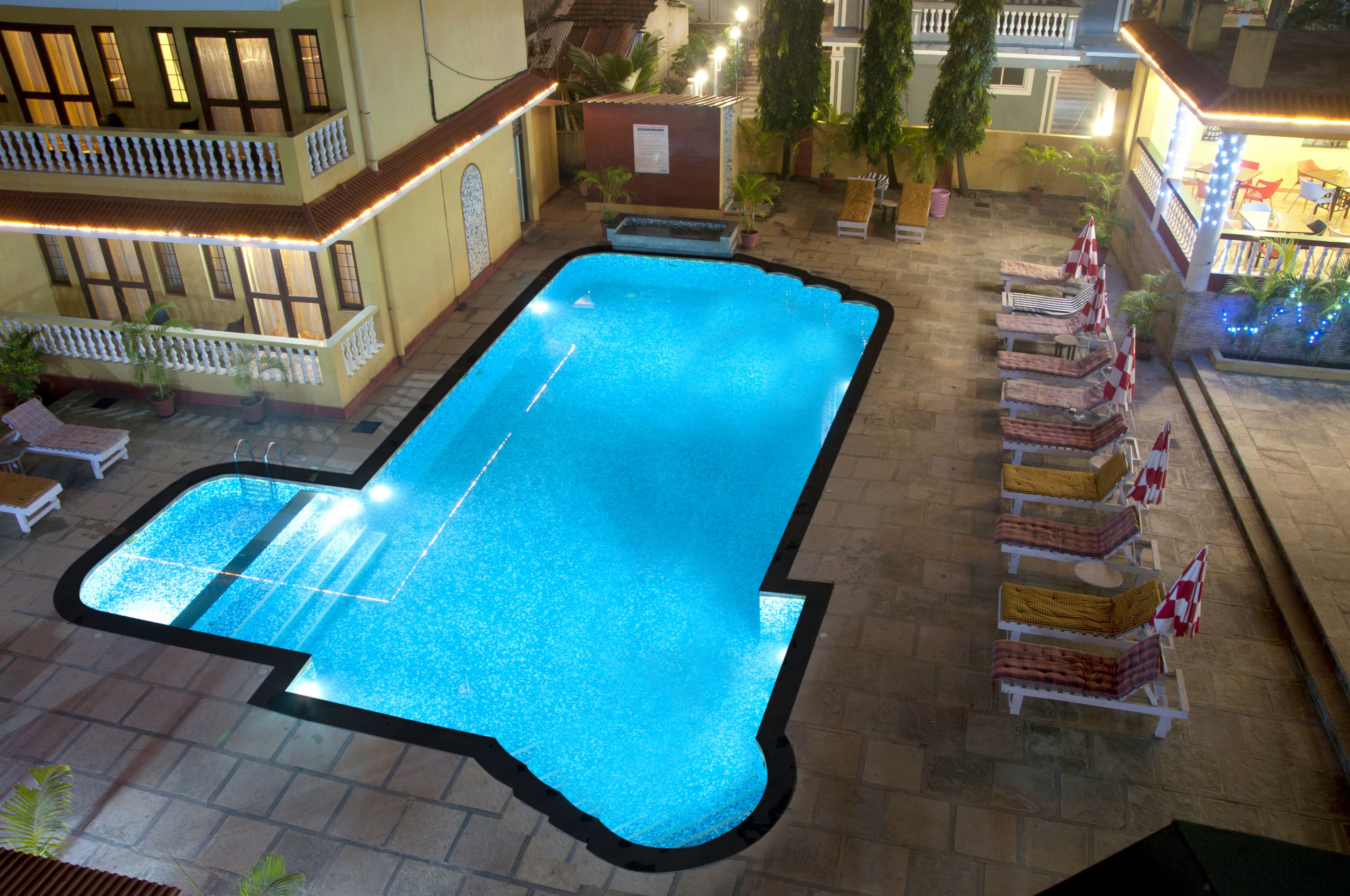 An indoor swimming pool with a tiled deck, surrounded by lounge chairs and potted plants.