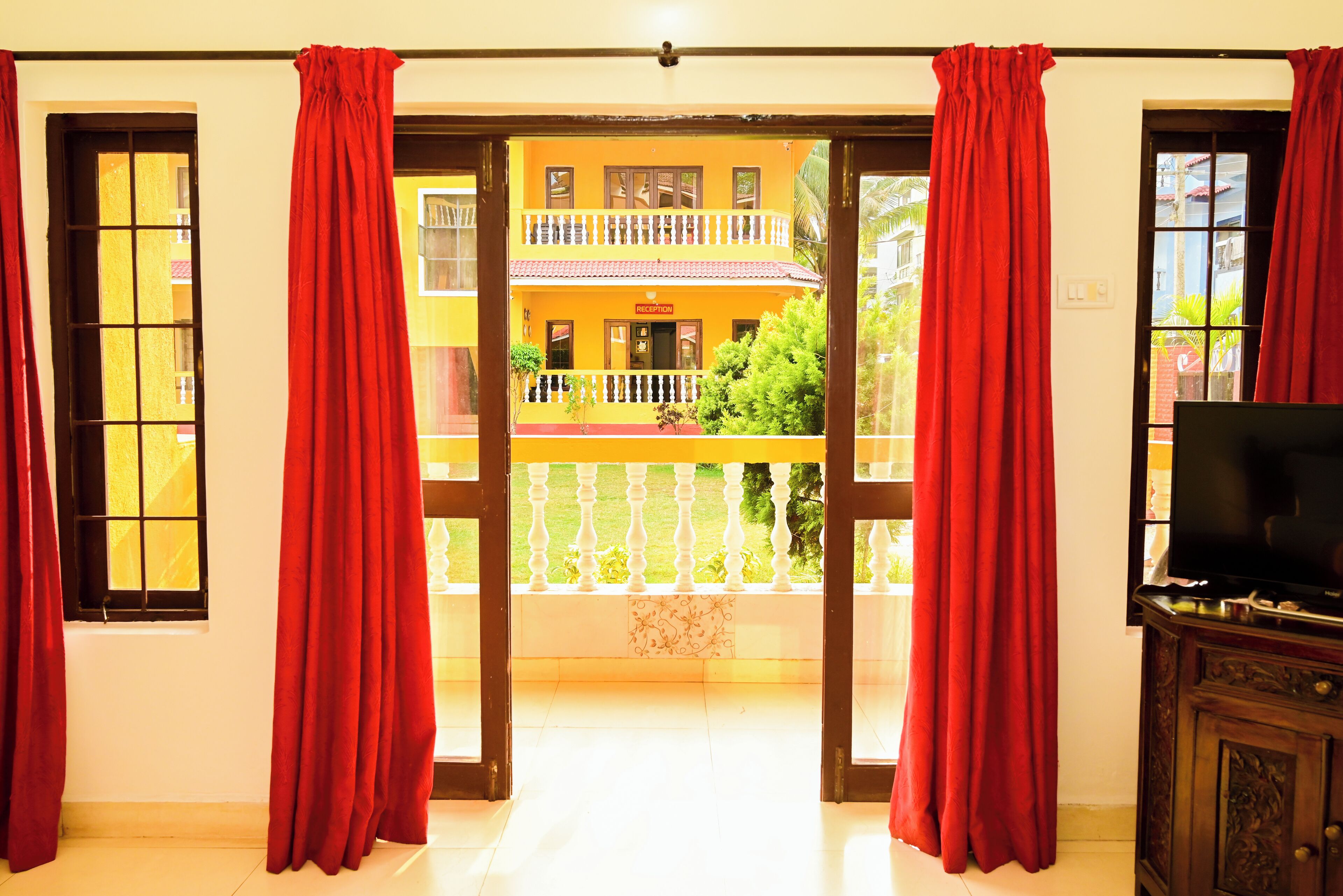 A room with a balcony, red curtains, a television, and a reception sign.