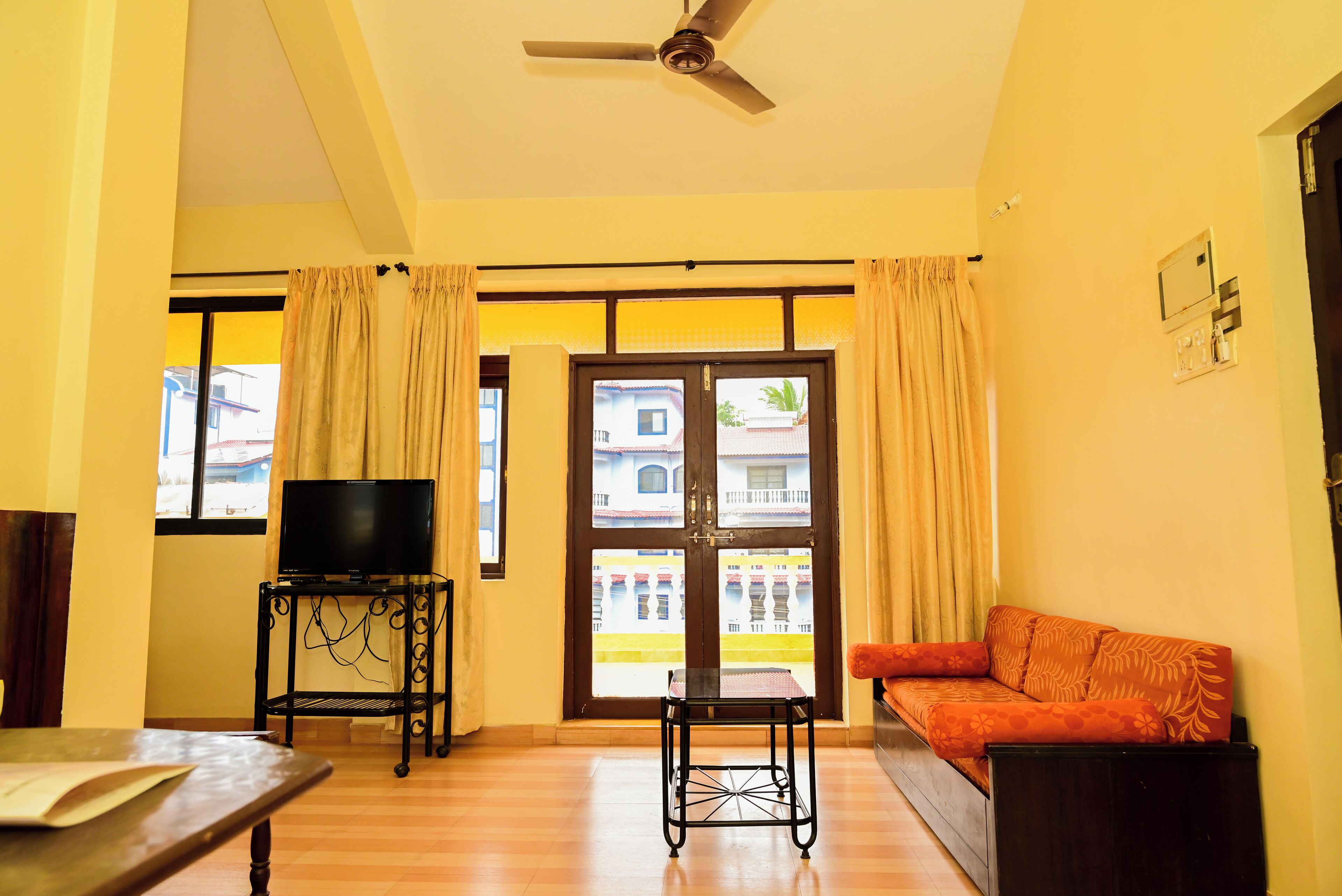 A living room with a sofa, a TV on a stand, a table, and a ceiling fan.