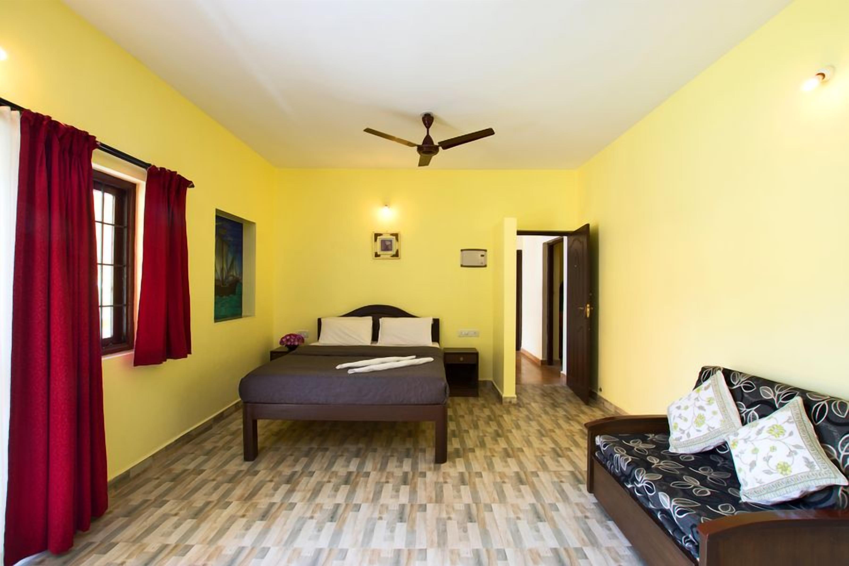 A bedroom with a bed, a nightstand, a sofa, a ceiling fan, and a window with curtains.