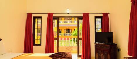 Ein Hotelzimmer mit Bett, Fernseher auf einem Schrank und einem Balkon mit roten Vorhängen.