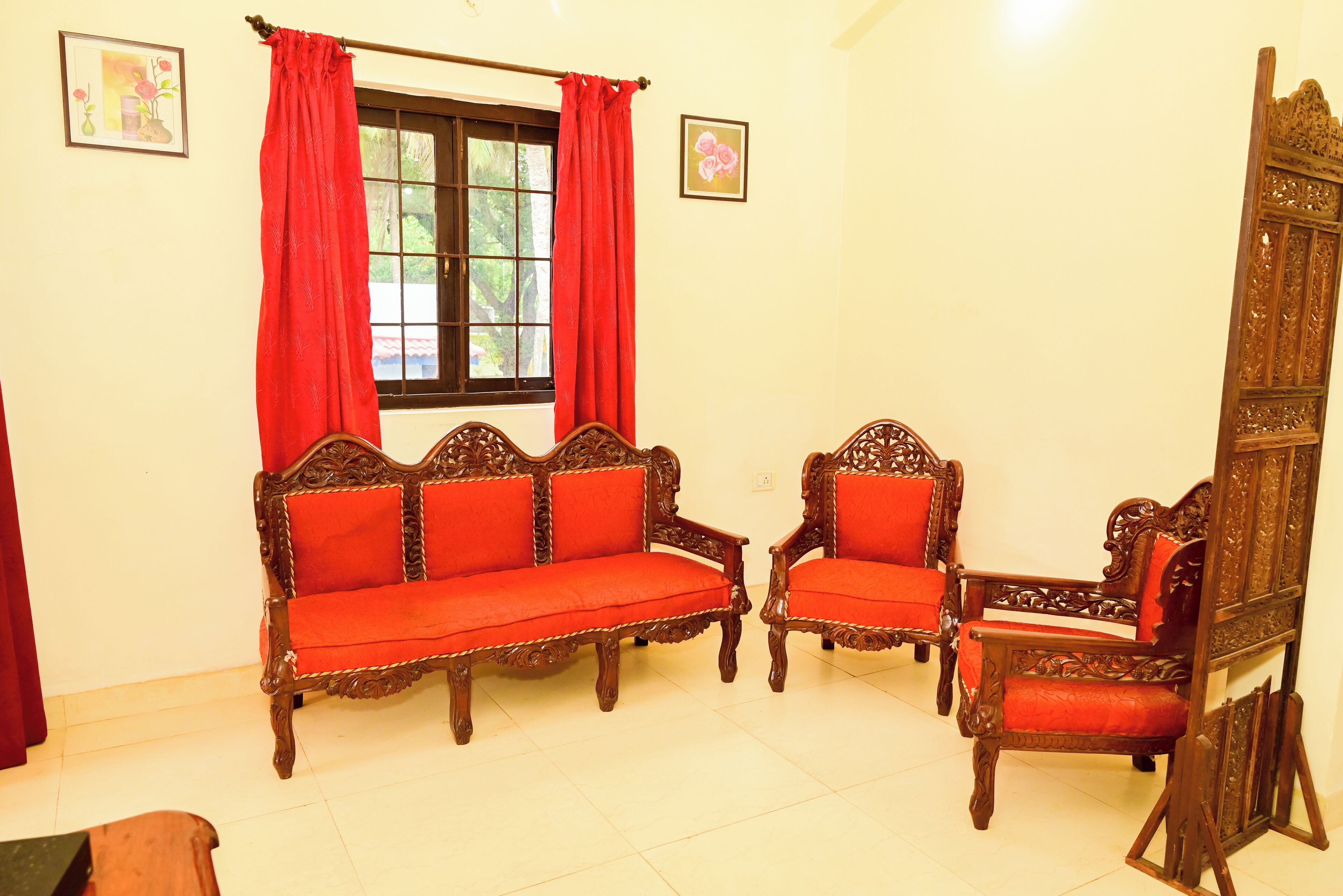 A room with a sofa, two armchairs, a wooden cabinet, and a window with red curtains.