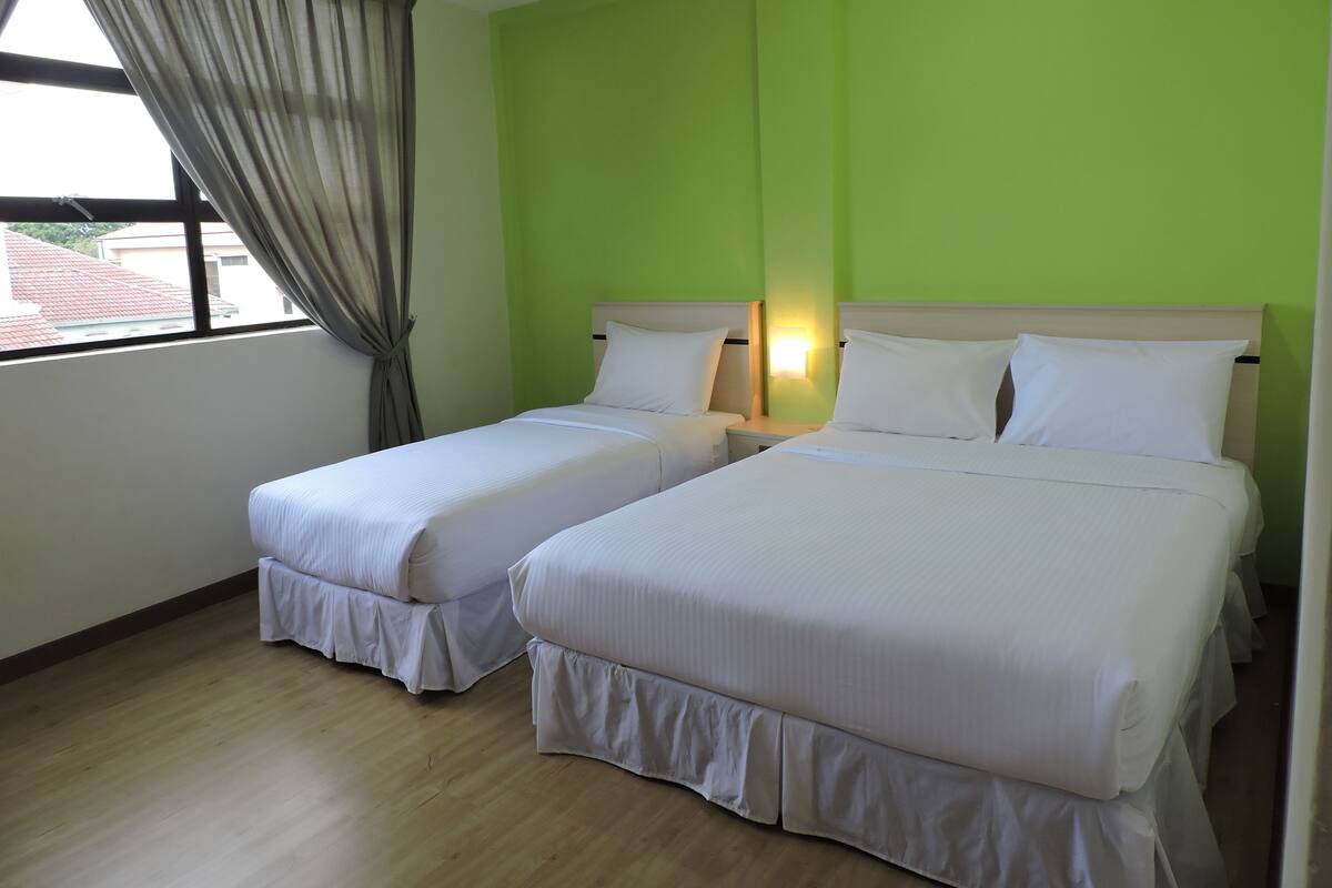 A hotel room with two single beds, a window with curtains, and a green wall.