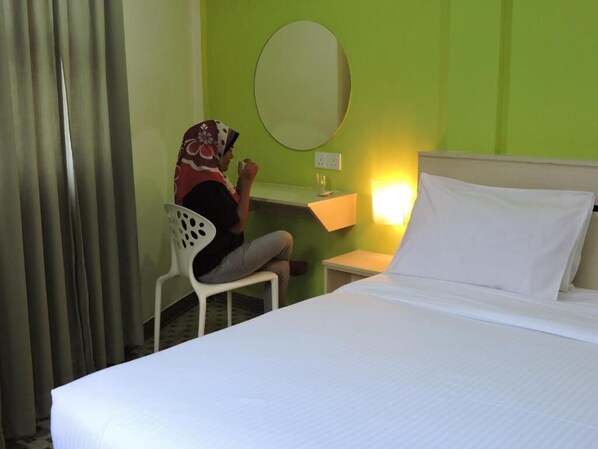 Une chambre d’hôtel équipée d’un lit, d’un bureau, d’une chaise, d’un miroir rond et d’une prise électrique murale.
