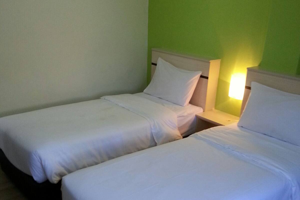 Two single beds with white linens in a room with green walls and wooden flooring.