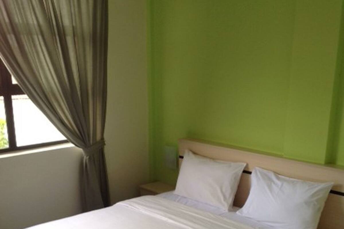 A bed with a white mattress and pillows, a wooden headboard, a nightstand with a lamp, and a window with curtains.