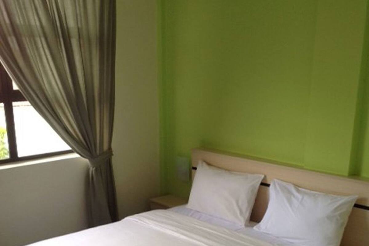 A single bed with a wooden headboard, a bedside table, and a window with curtains.