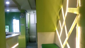 A hallway with a reception desk, a green bench, and patterned flooring. - Merlin Hotel (George Town)