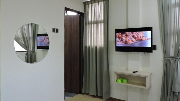 A modern living room with a flat-screen TV mounted on the wall, a round mirror, and a wooden door. - Merlin Hotel (George Town)