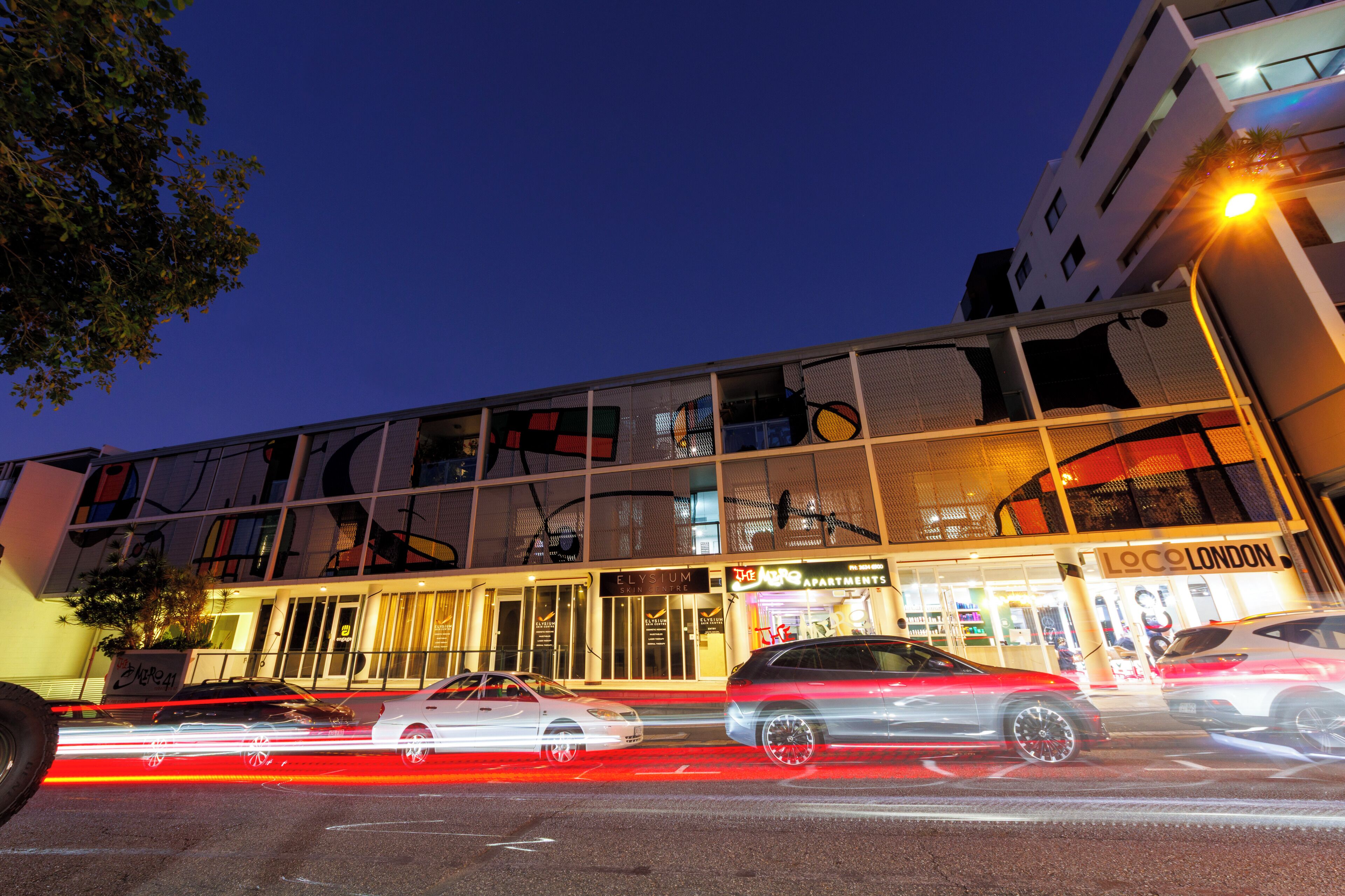 A modern building with a glass facade, a sign for 'Elysium Apartments', and a 'Loc London' sign.