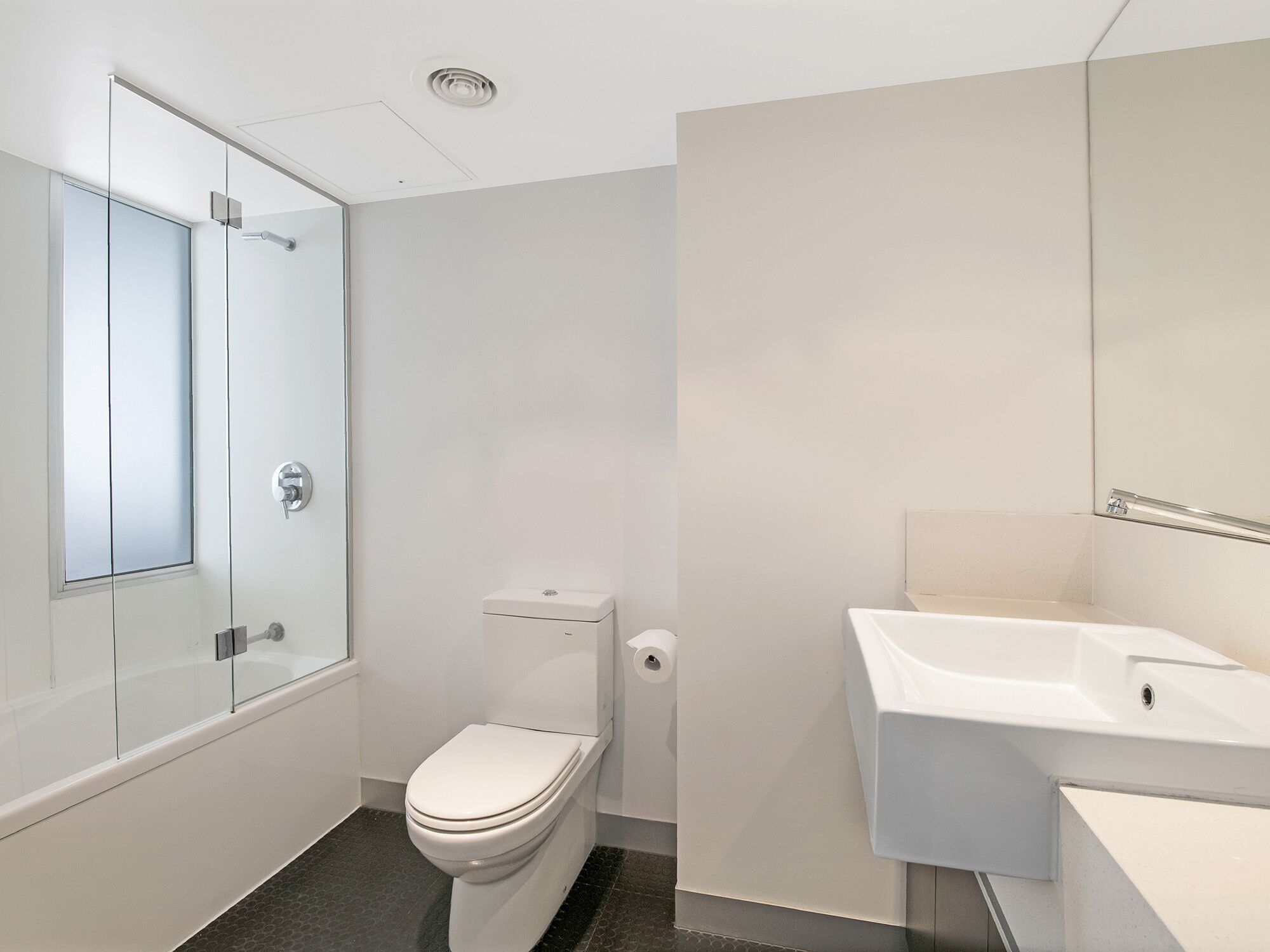 A modern bathroom with a toilet, a glass shower enclosure, and a sink.