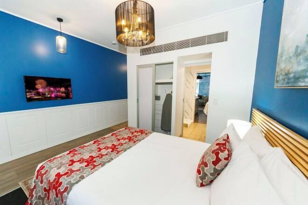 A hotel room with a bed, a television, a chandelier, and a blue accent wall.