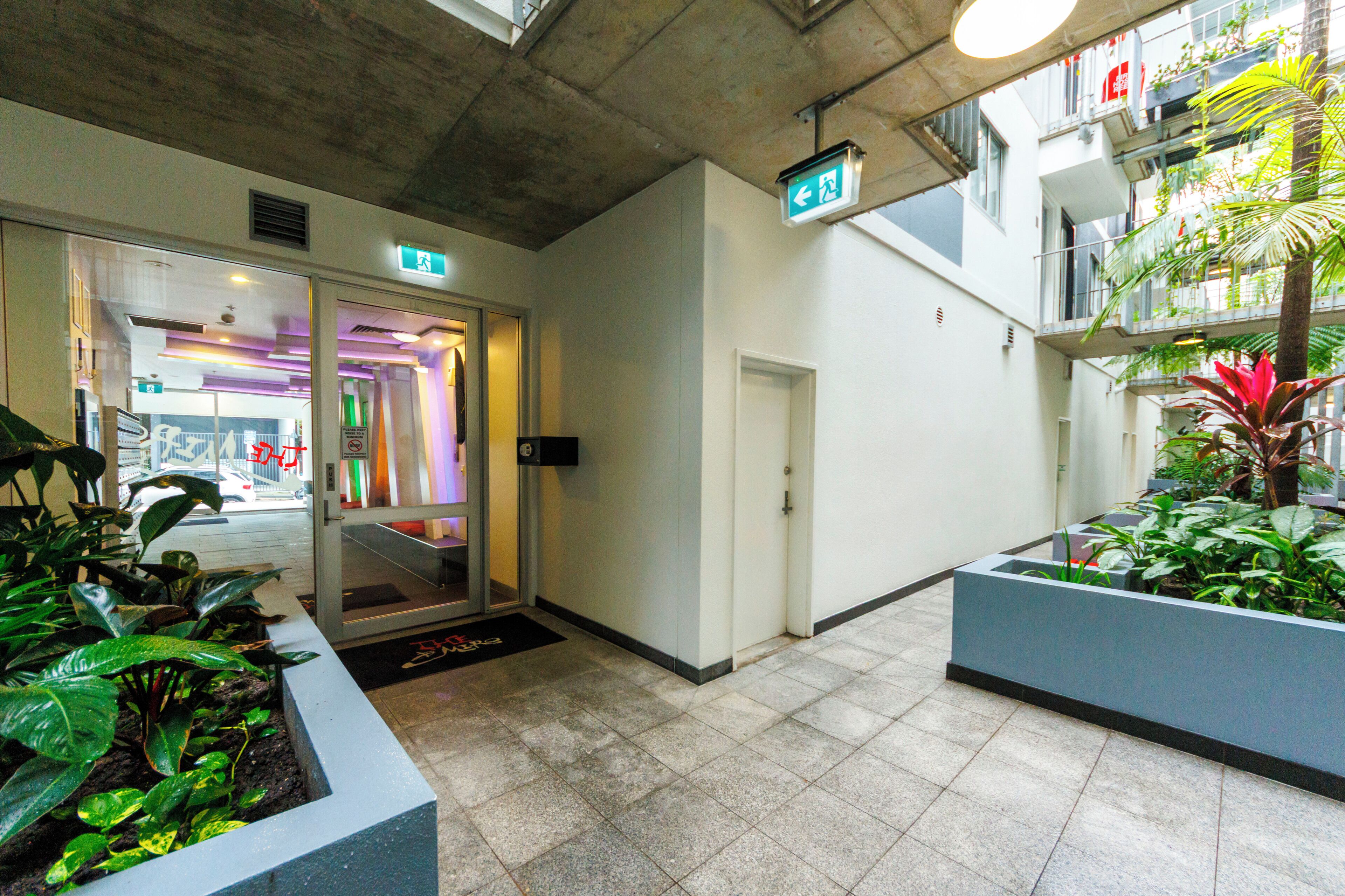 A modern indoor space with a glass door entrance, a visible exit sign, and potted plants.