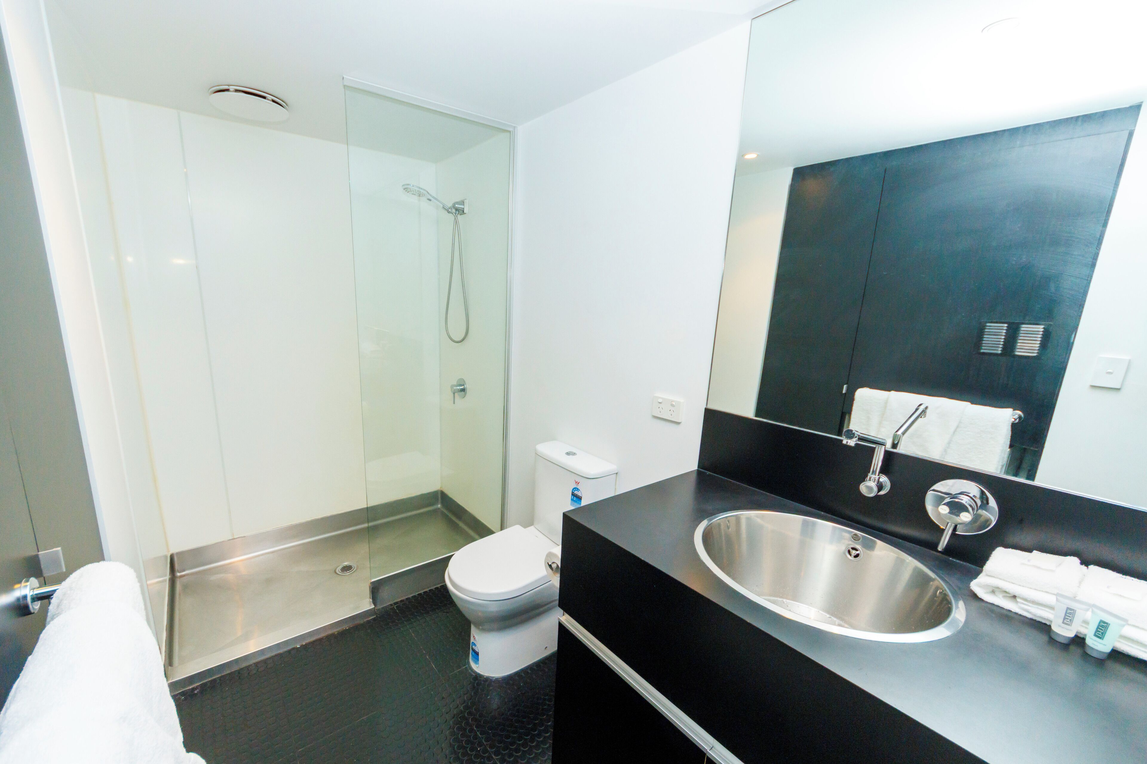 A modern bathroom with a glass-enclosed shower, a stainless steel sink, and a white toilet.