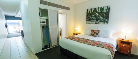 A hotel room with a large bed, a wardrobe, a bedside table with a lamp, and a painting on the wall.