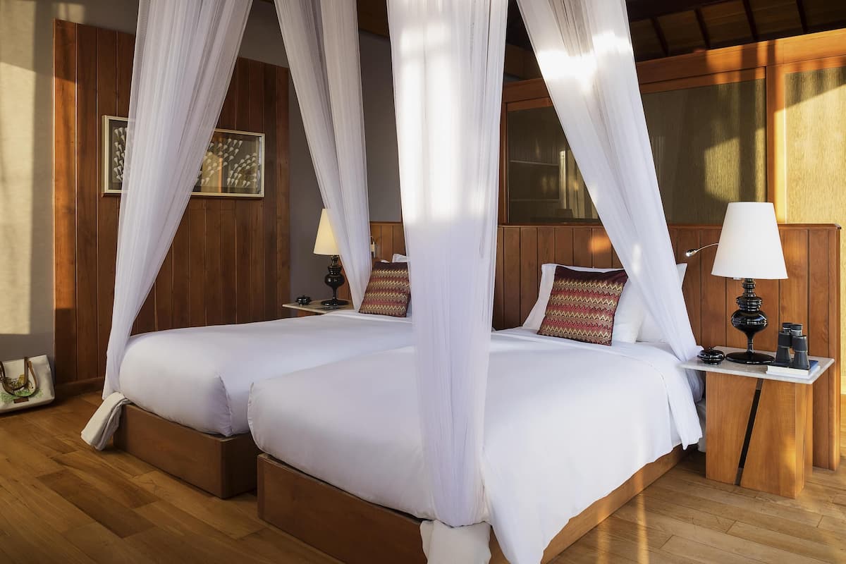 A four-poster canopy bed with a wooden headboard, bedside tables with lamps, and a wooden floor.