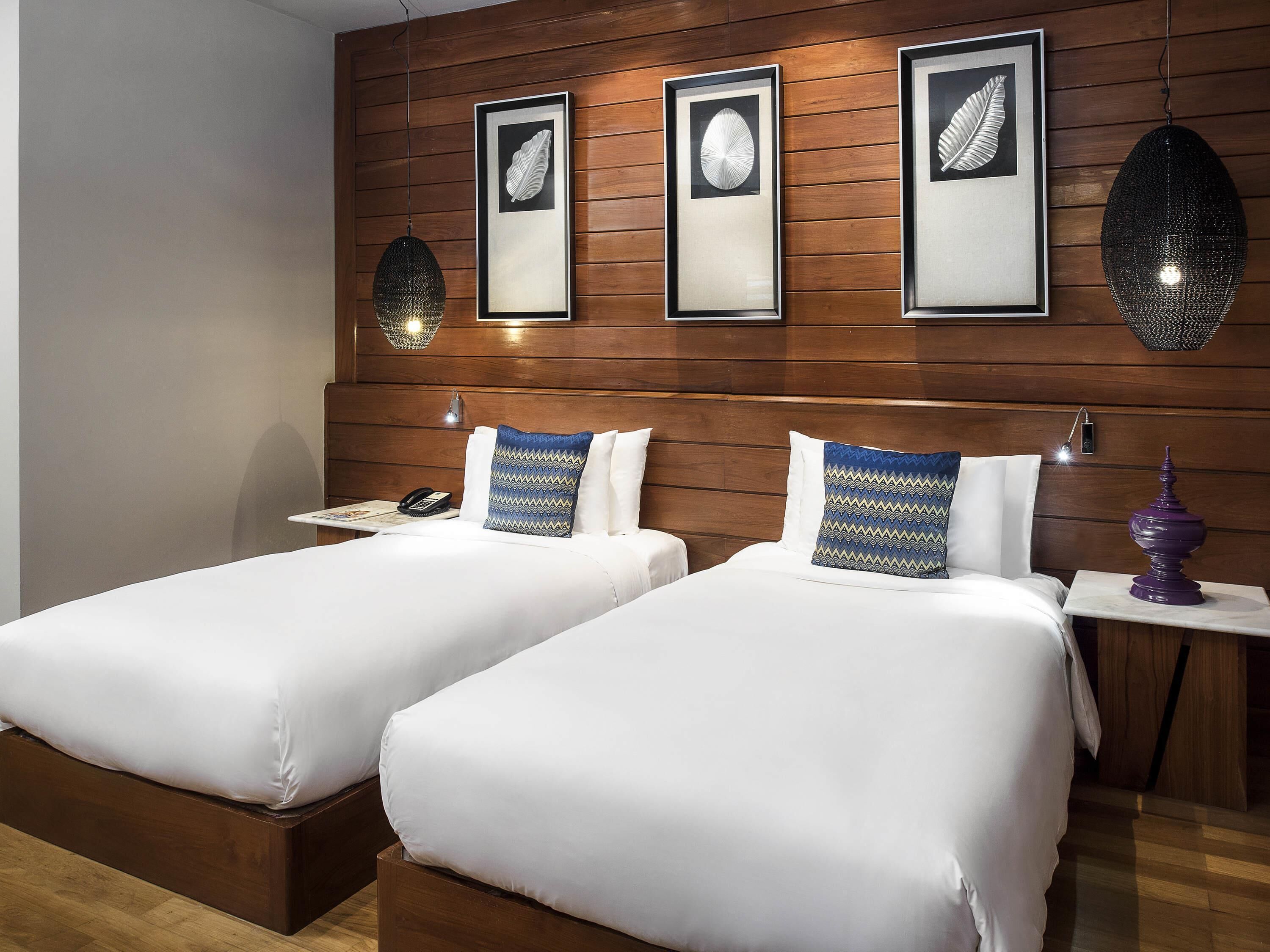 A hotel room with two beds, wooden headboard, framed artwork, bedside lamps, and a nightstand with a lamp.