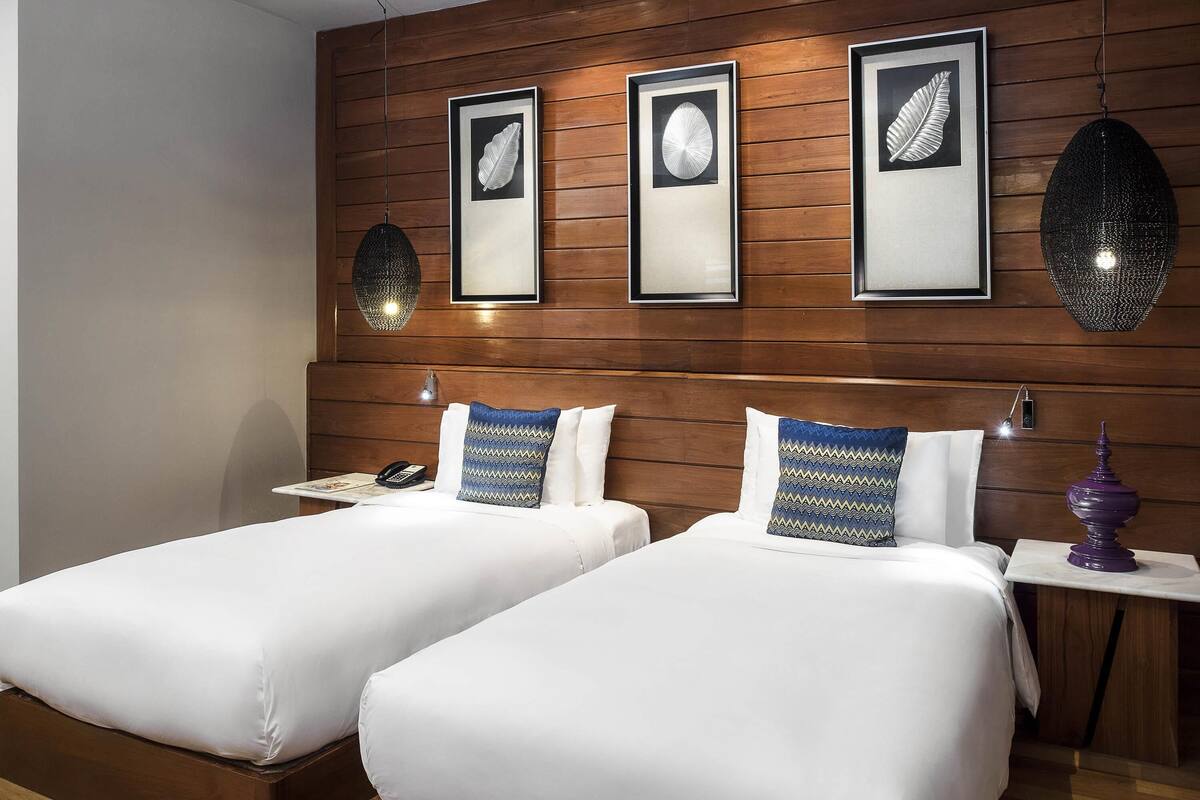 Quarto de hotel com duas camas, cabeceira de madeira, obra de arte emoldurada, luminárias de cabeceira e mesa de cabeceira com abajur.