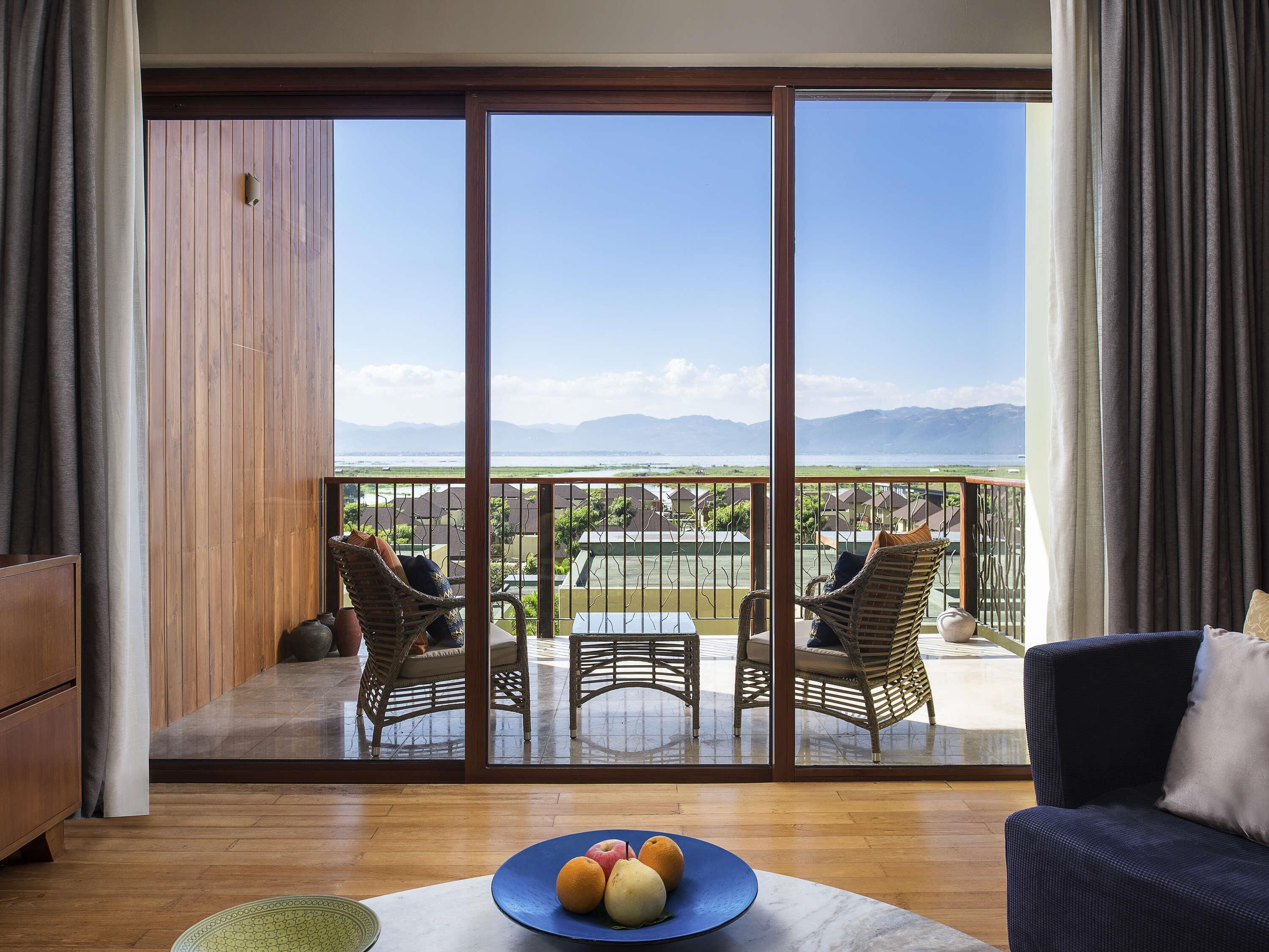 A room with a large sliding glass door leading to a balcony with wicker furniture and a view of a coastal landscape.