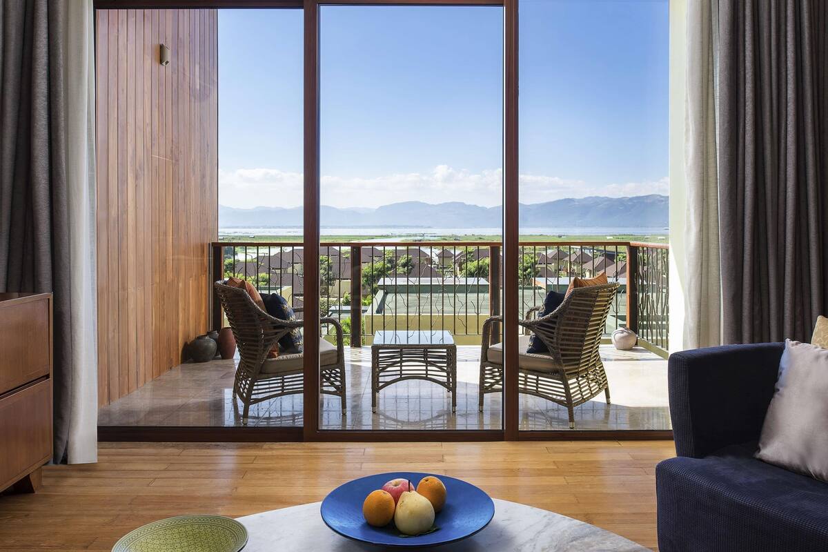 Quarto com uma grande porta de vidro deslizante que dá para uma varanda com mobiliário de vime e vista para a paisagem costeira.