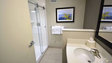 A modern bathroom with a glass shower, a sink with a mirror, and a framed picture on the wall.