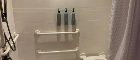 A modern bathroom with a white bathtub, a showerhead, a towel rack, and three bottles of shampoo.
