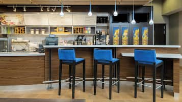 Una cafetería con un mostrador de madera, tres taburetes azules y una pizarra con la carta.