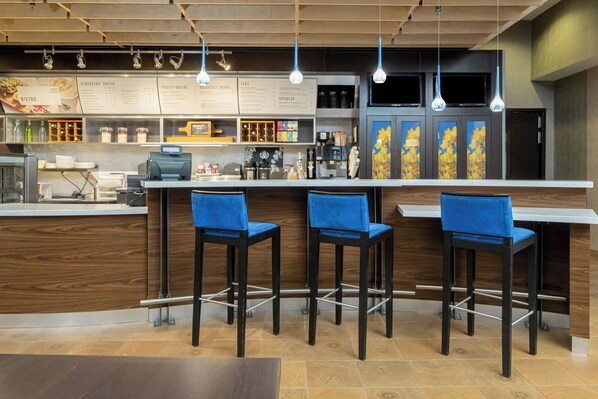 A café with a wooden counter, three blue bar stools, and a menu board above.
