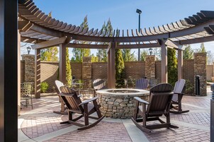 Un patio con un pozo de fuego de piedra, sillas de madera mecedoras y una pérgola.