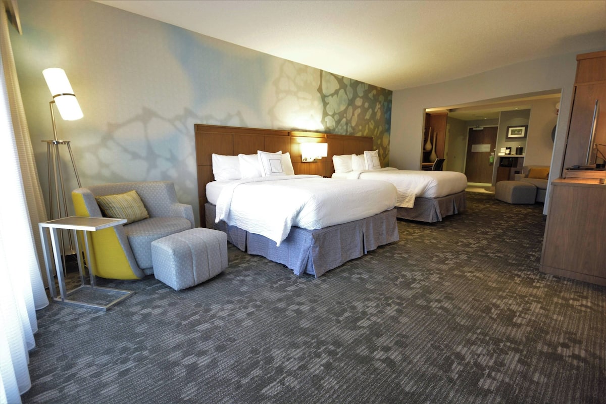 Une chambre d’hôtel avec deux lits, un canapé, une petite table et une lampe.