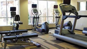 Une salle de sport équipée de tapis de course, de vélos elliptiques et de bancs de musculation.