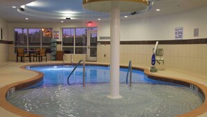 An indoor pool with a central column, a lifeguard station, and a seating area with chairs.
