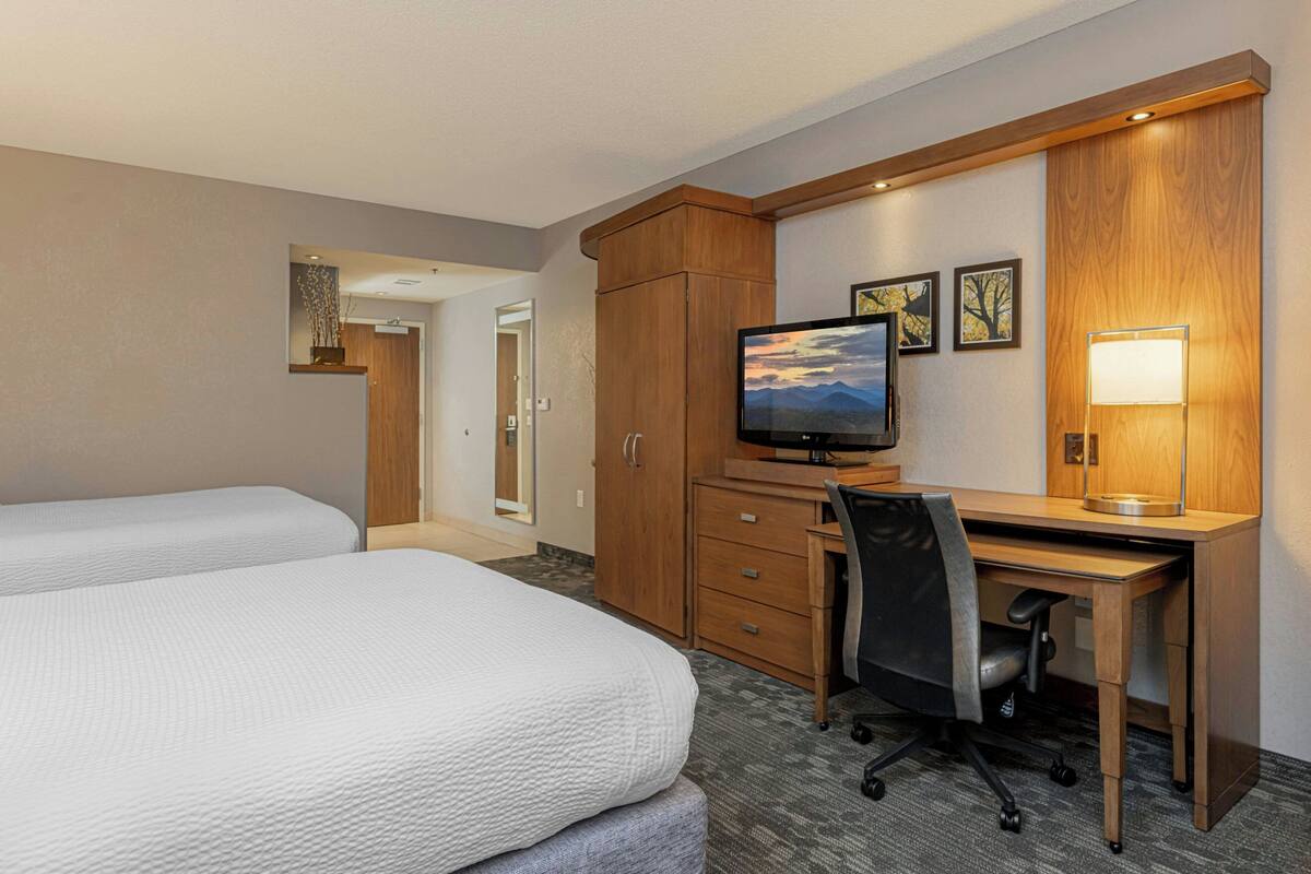 Une chambre d’hôtel avec deux lits, un bureau, une chaise, une télévision et une lampe.