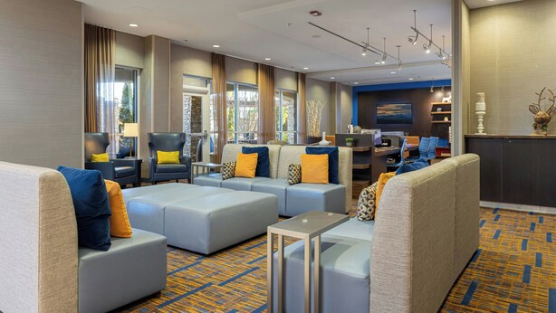 A modern hotel lobby with seating areas, a reception desk, and a view of the outdoors.
