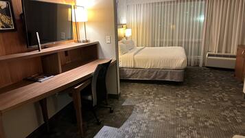 Habitación de hotel con cama, escritorio, silla, televisor y lámparas.