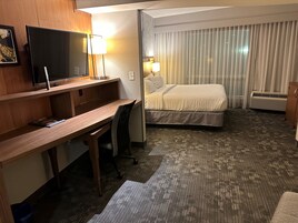 Habitación de hotel con cama, escritorio, silla, televisor y lámparas.