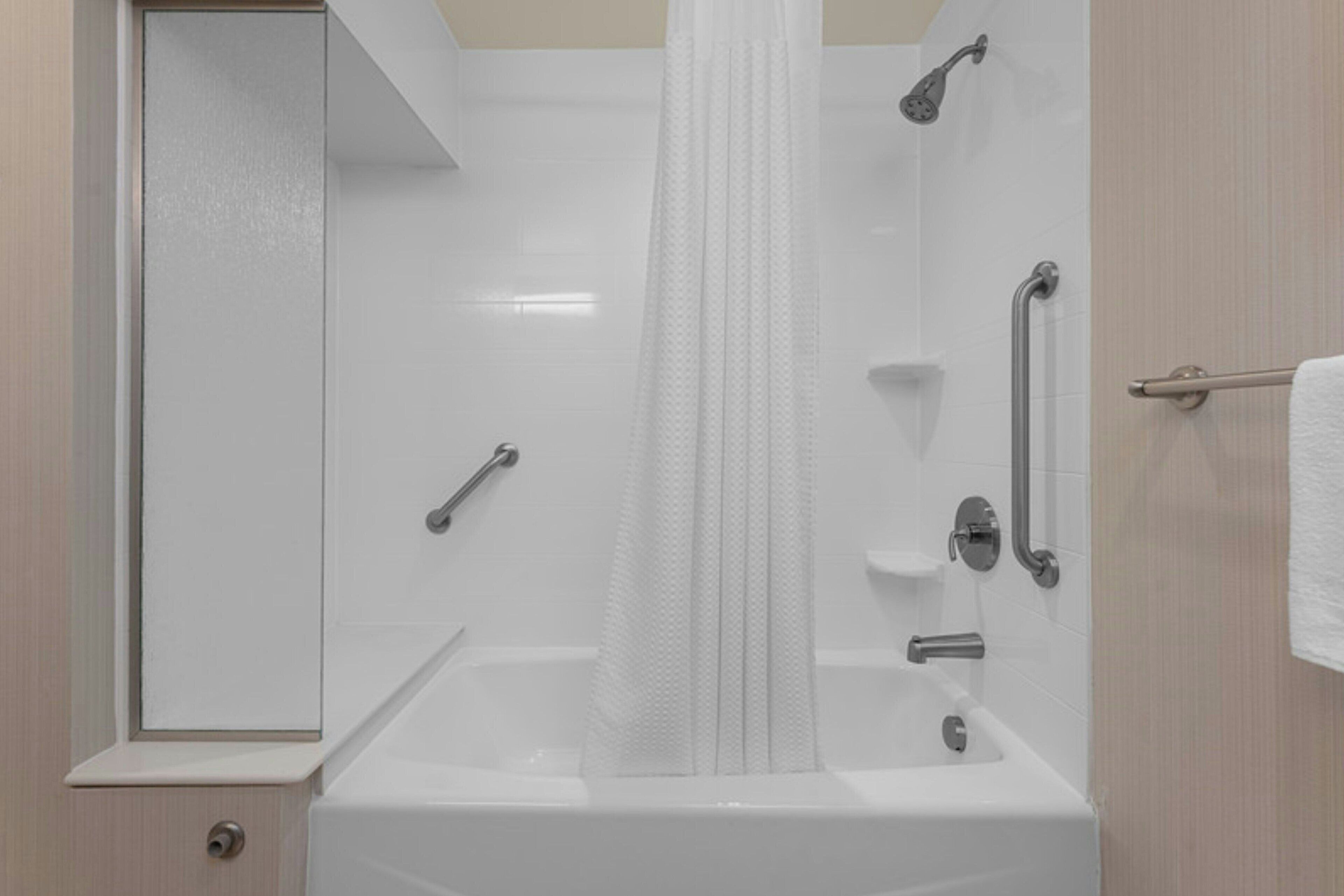 A modern bathroom with a bathtub, shower, and handrails.
