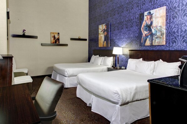 A hotel room with two beds, a desk, a chair, and artwork on the walls.