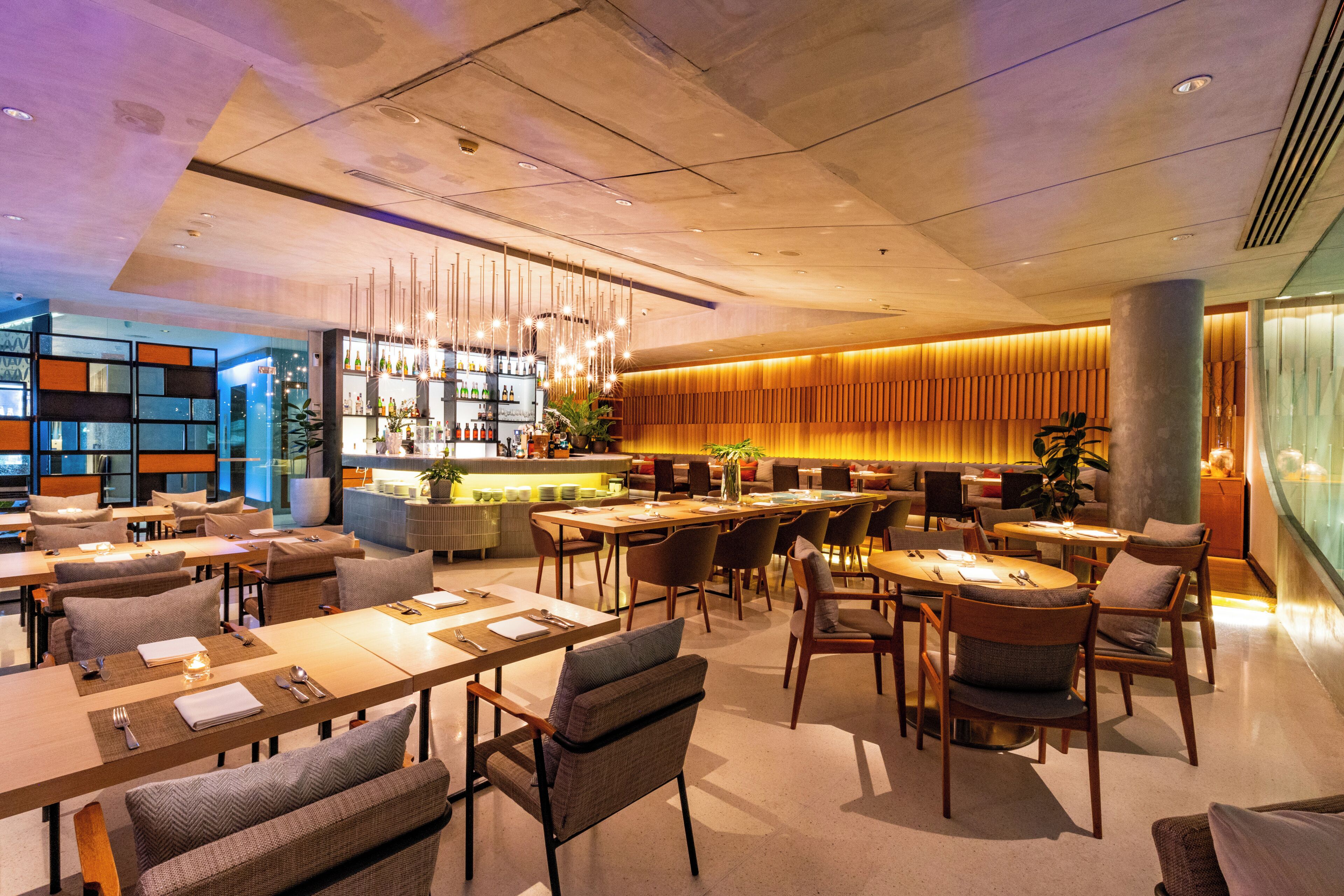 A modern restaurant with multiple dining tables and chairs, a bar area, and a seating section with sofas.