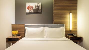 A hotel room with a bed, two bedside tables, a nightstand with a vase of flowers, a wall-mounted picture, and a bedside lamp.